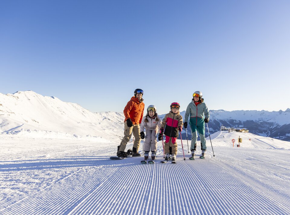 Eine Familie posiert auf einer Piste im Schnee beim Skifahren.