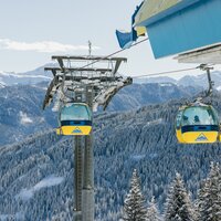 Seilbahn mit bunten Kabinen fährt über schneebedeckte Berge.