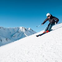 Skifahrer auf verschneiter Piste mit Bergen im Hintergrund.