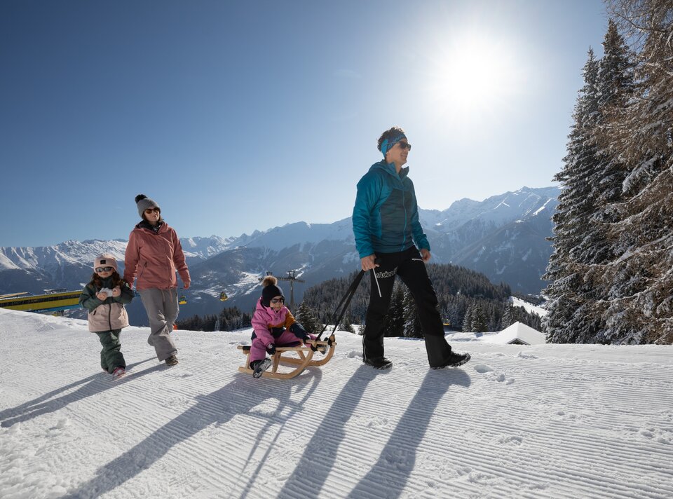 Eine Familie beim Schlittenfahren in den Bergen an einem sonnigen Tag.