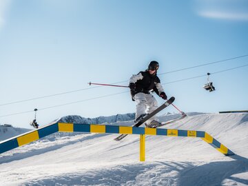 A skier performing a jump over a rail on snow.