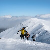 Drei Skitourengeher erklimmen einen schneebedeckten Berg.