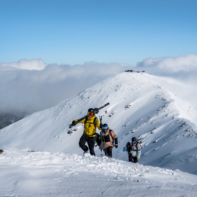 Drie skitoeristen beklimmen een met sneeuw bedekte berg.