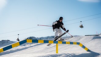 A skier performing a jump over a rail on snow.