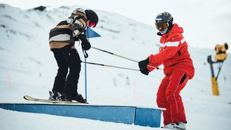 A coach assists a child skiing on a box.