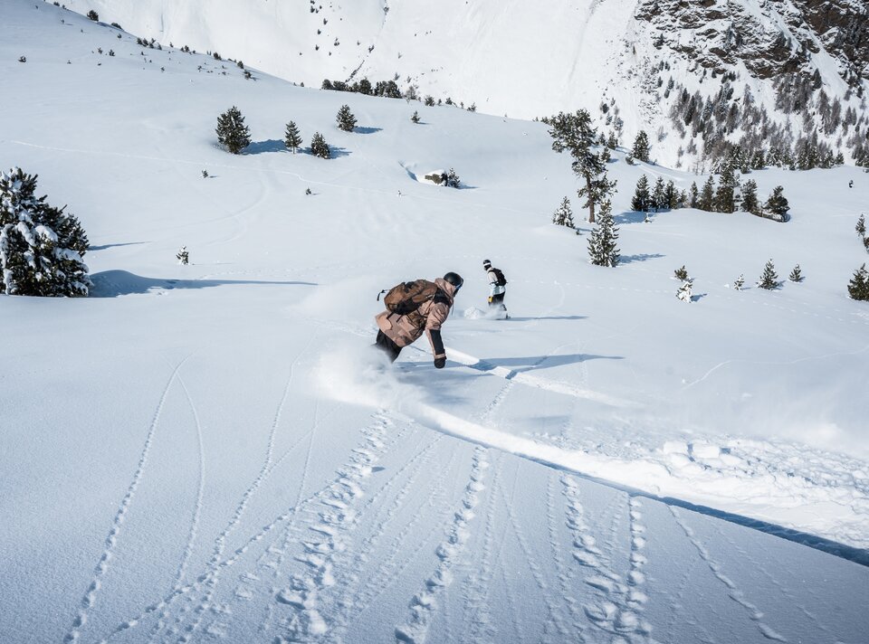 Twee personen snowboarden door diepe poedersneeuw in de bergen.