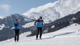 Two skiers practicing cross-country skiing on a snowy trail.