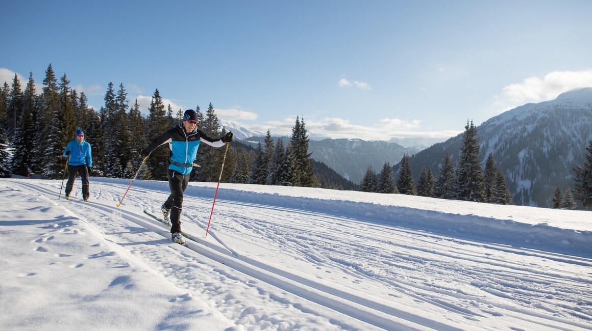 Zwei Sportler beim Langlaufen in einer verschneiten Landschaft.