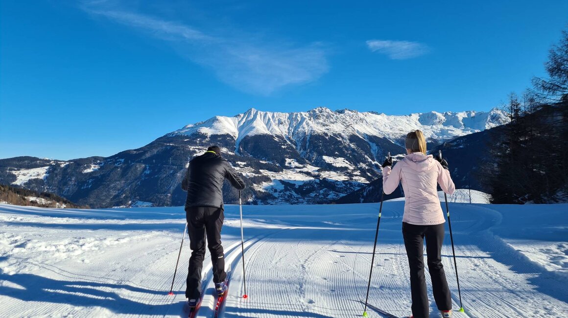 Zwei Skifahrer auf präparierter Loipe mit Bergpanorama.