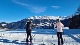 Zwei Skifahrer auf präparierter Loipe mit Bergpanorama.