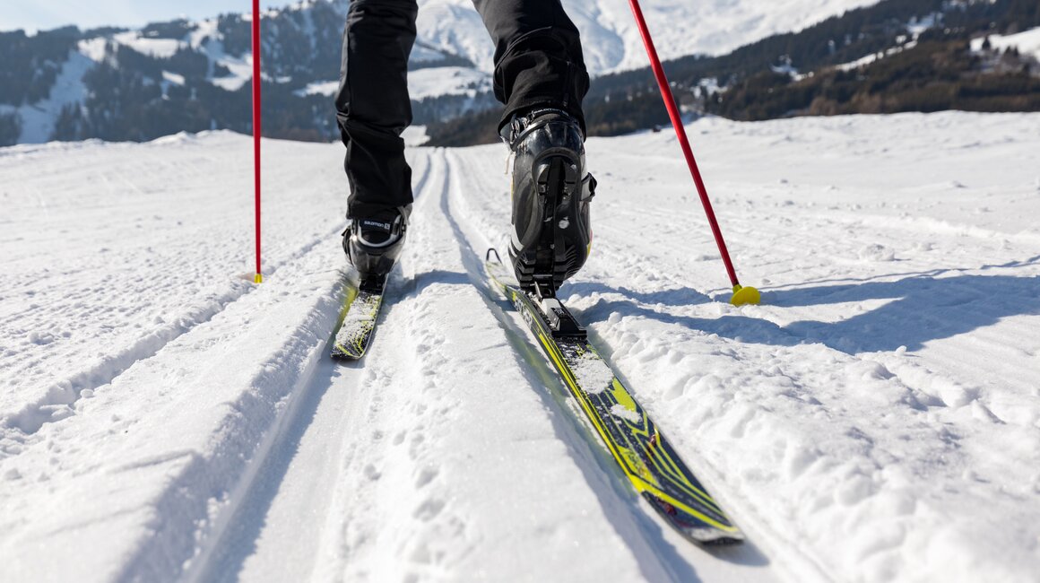 Person, die auf einem klaren Skiweg in der verschneiten Landschaft skifährt.