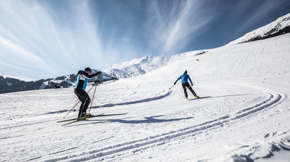 Zwei Skifahrer gleiten über eine schneebedeckte Landschaft.