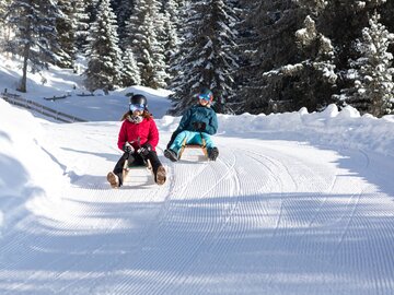 Two kids are sitting on sleds in a snowy landscape.