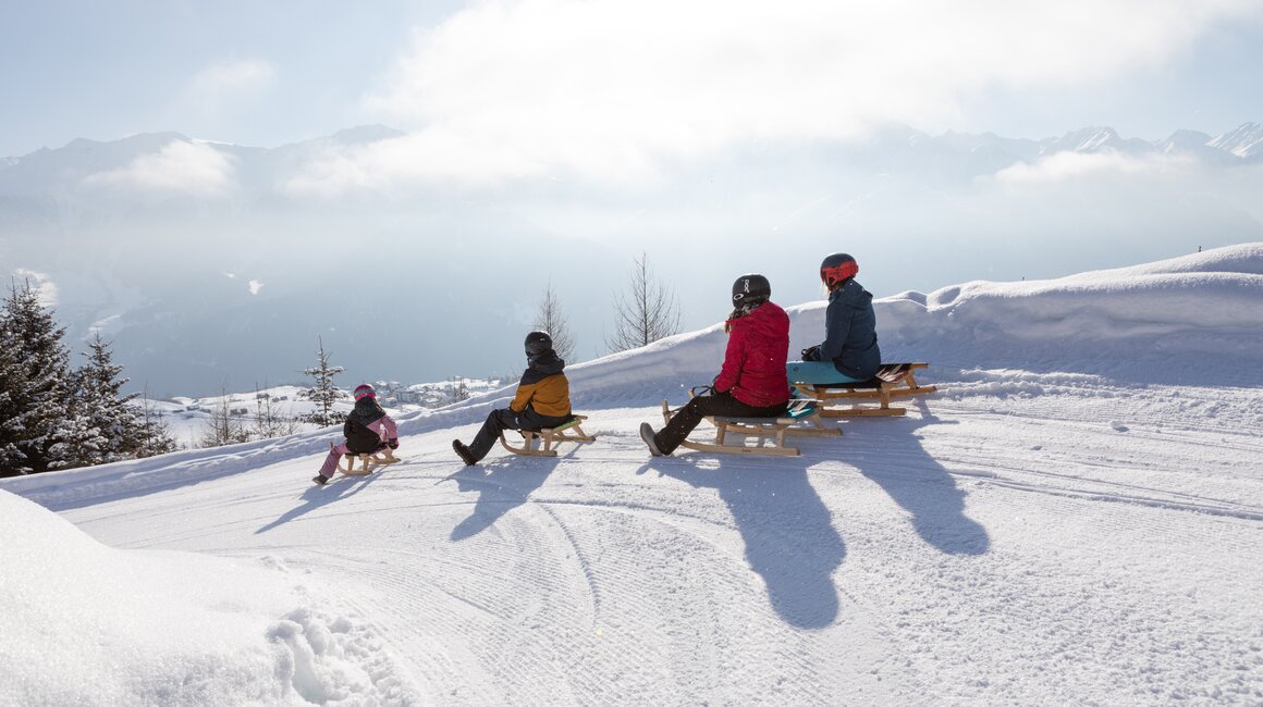 Eine Familie sitzt auf Schlitten im Schnee und genießt den Ausblick.