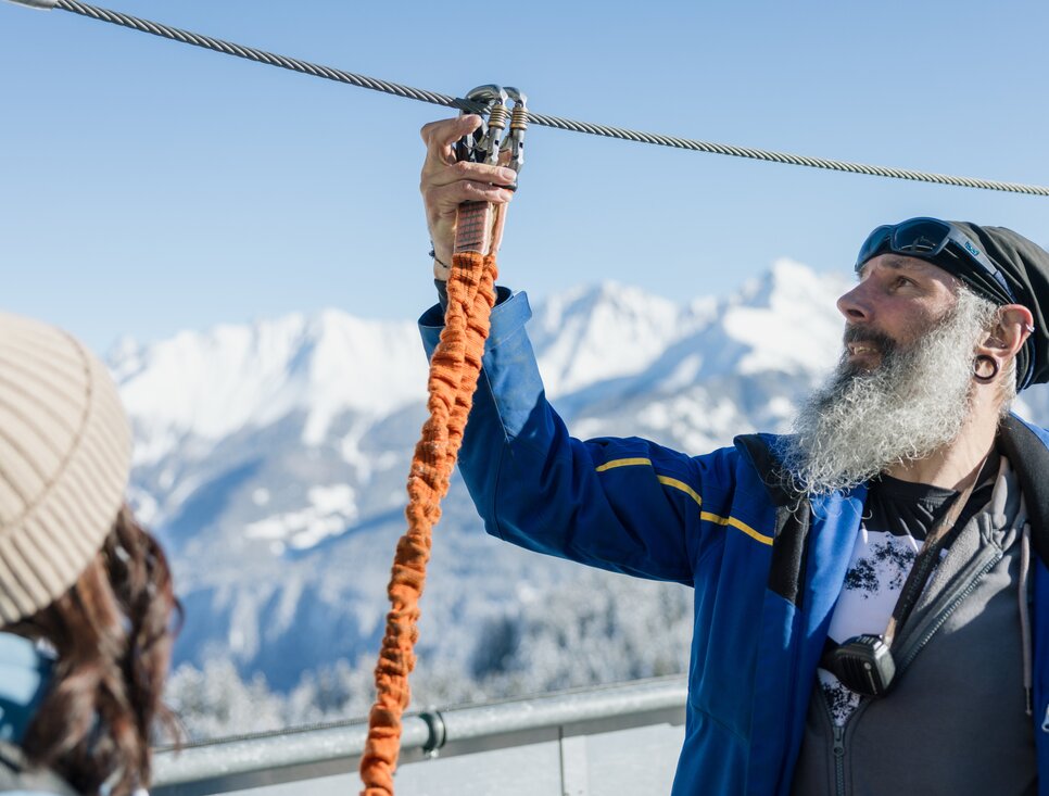 A man explains the zipline equipment in the Alps.