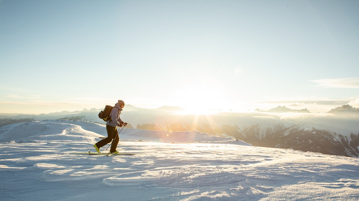 Ein Skifahrer wandert auf verschneiten Bergen bei Sonnenaufgang.