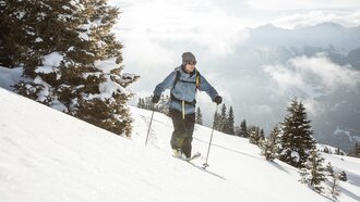 Ein Skifahrer fährt durch schneebedeckte Berge unter einem blauen Himmel.