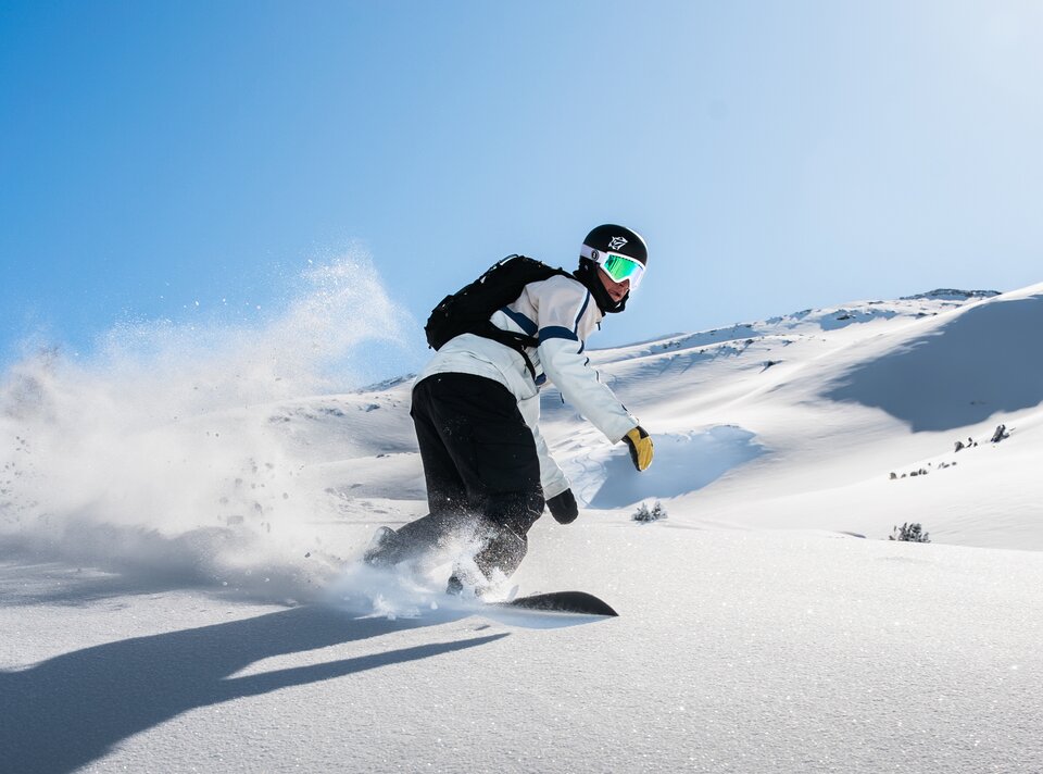 Een snowboarder glijdt door verse sneeuw onder een blauwe lucht.