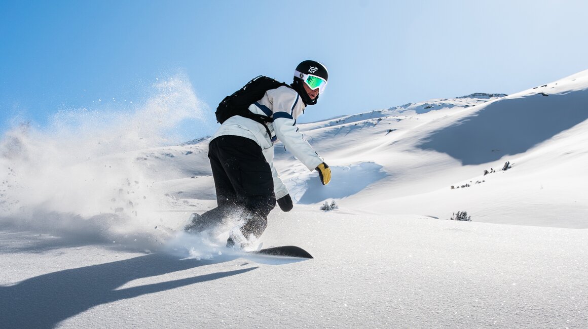 Ein Snowboarder fährt durch frischen Schnee unter blauem Himmel.