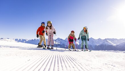 A family of four skiing together under a clear blue sky.