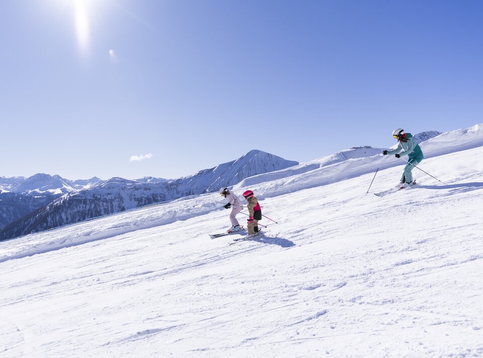 Drei Skifahrer, darunter zwei Kinder, genießen den Schnee in den Alpen.