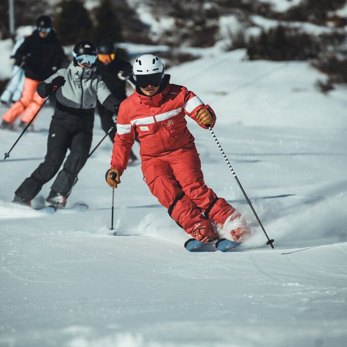 Skiers in red gear gliding down a snow-covered slope.