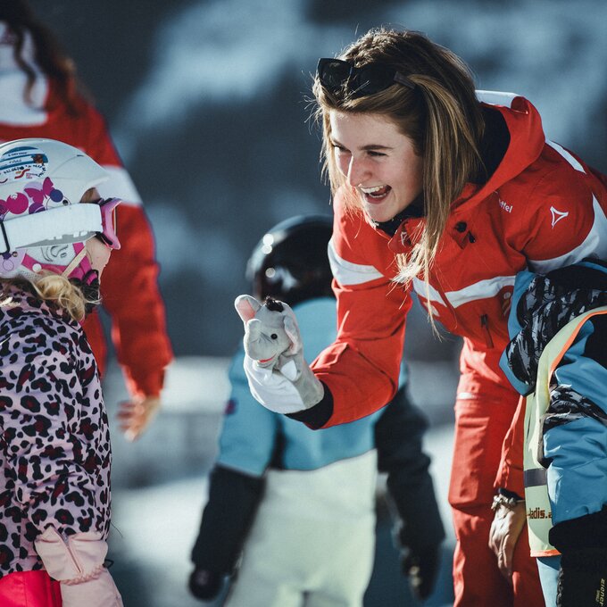 A ski instructor shows a child a toy while teaching skiing.