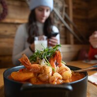 Ein Meeresfrüchte-Gericht mit Garnelen und Gemüse, während eine Person im Hintergrund am Handy ist.