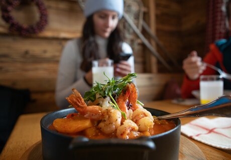 A seafood dish with shrimp and vegetables, while a person in the background is on their phone.