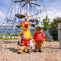Fröhliche Kinder posieren mit zwei bunten Maskottchen auf einem Spielplatz.