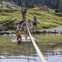 Two kids on a raft in the water with parents in the background.