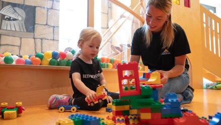 A child and a caregiver are playing with building blocks in a colorful playroom.