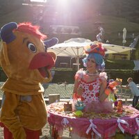 Ein Clown und ein Maskottchen interagieren unter Sonnenschein.