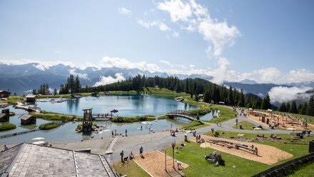 Families enjoy the day at a mountain lake with a playground and nature.