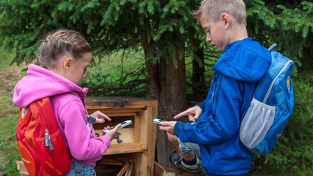 Two kids with backpacks using smartphones outdoors.