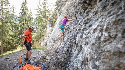 A person climbs a rock wall while a partner secures them.