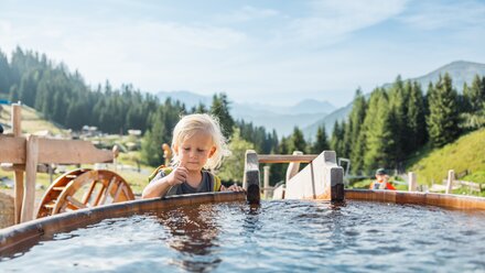 A child examines the water in a wooden basin with mountain scenery.