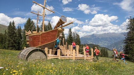 Family playing on a wooden ship playground in the Alps.