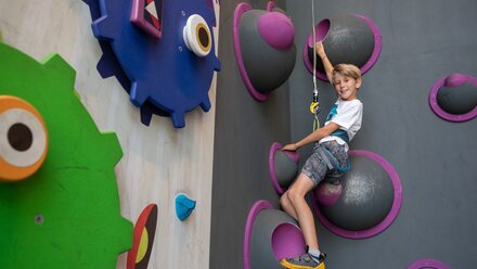 A boy is climbing a colorful climbing wall with big holds.