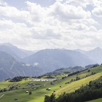 Blick auf grüne Wiesen und Berge unter bewölktem Himmel.