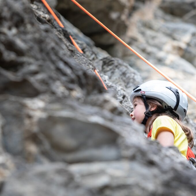 A girl in a helmet climbs a rock wall secured by ropes.