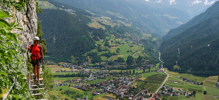Kletterer an einem steilen Hang mit Blick auf ein Tal.