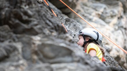 A girl in a helmet climbs a rock wall secured by ropes.