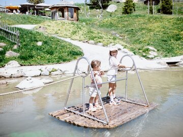 Zwei Kinder genießen das Spielen auf einem Floß in einem kleinen Gewässer.