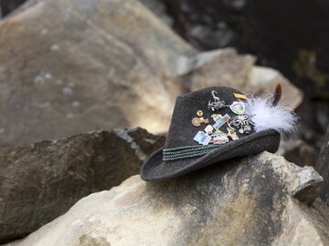 Ein Trachtenhut, geschmückt mit verschiedenen Pins, liegt auf Felsen.