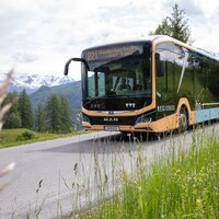 A MAN bus driving on a road with mountains in the background.