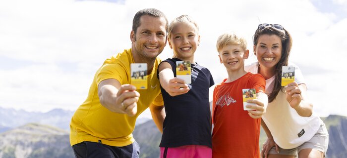 A happy family poses outdoors holding cards in their hands.