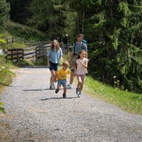 Eine Familie mit Kindern wandert fröhlich auf einem schottrigen Weg.