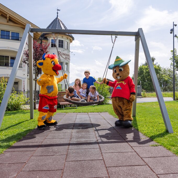 Two mascots and kids on a swing in a park.