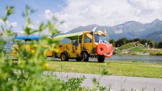 Een kleurrijk voertuig met dierenontwerp aan de oever van een waterpartij.